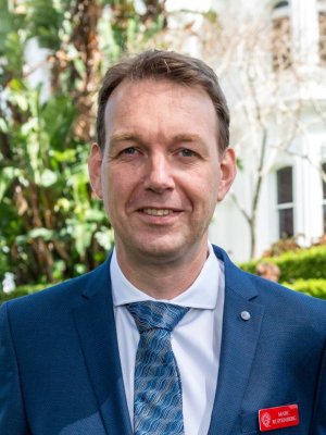 Associate Professor Marc Ruitenberg says his Churchill Fellowship will allow him to visit some of the world's leading laboratories in 2023. A man in a tie, white shirt and blue jacket smiles. He is outdoors with a building and tree in the background.